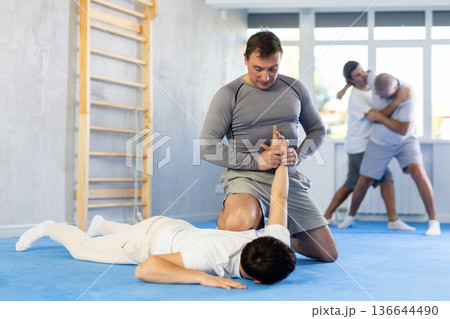 Guy and man are training in gym practicing technique of grabbing arm and lowering opponent to floor 136644490