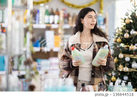 Young girl choosing dishwashing liquid in store with New Year decoration Young girl choosing dishwashing liquid in store with New Year decoration 136644518