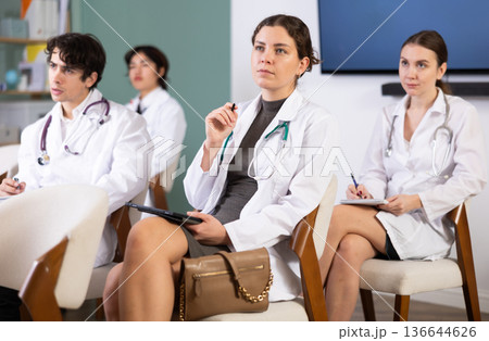 Focused group of medicals students sitting on chairs and listening lecture, taking notes on tablet in lecture hall Focused group of medicals students sitting on chairs and listening lecture, taking notes on tablet in lecture hall 136644626