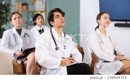 Young female doctor listening and taking notes in lecture hall Young female doctor listening and taking notes in lecture hall 136644753