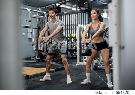 Fitness trainer coach man teaching and holding kettlebell exercising with asian woman client in gym. Fitness trainer coach man teaching and holding kettlebell exercising with asian woman client in gym. 136648200