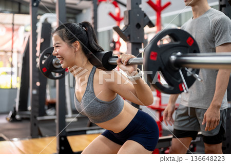 Asian woman client exercising with weight lift barbell while fitness gym trainer coach man observing 136648223