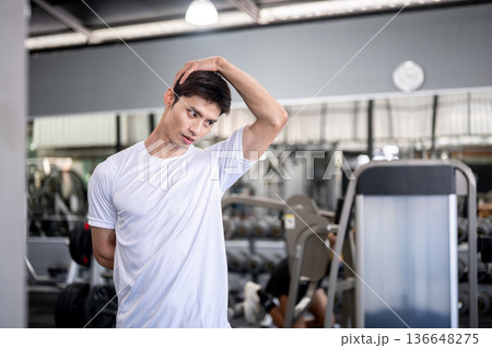 Asian man fitness trainer or a client standing and stretching neck aside exercise equipments in gym. 136648275