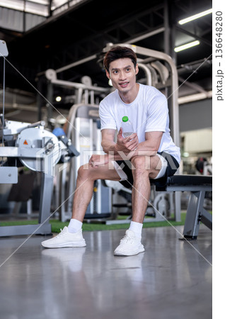 Asian man client fitness trainer coach sitting holding water bottle resting after exercising in gym. Asian man client fitness trainer coach sitting holding water bottle resting after exercising in gym. 136648280