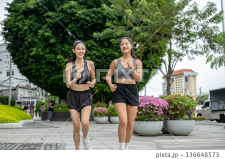 Asian woman friends in sportswear exercising by running or jogging on pavement in mall's garden park Asian woman friends in sportswear exercising by running or jogging on pavement in mall's garden park 136648573