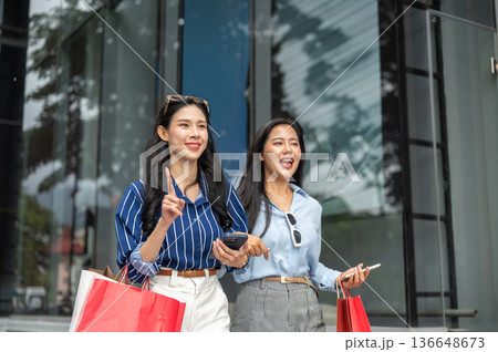 Pretty asian woman and friend carrying shopping bag talking walking together outside a shopping mall 136648673