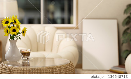 Sunflower vase and coffee cup on glass table across sofa and canvas frame on floor in a living room 136648718