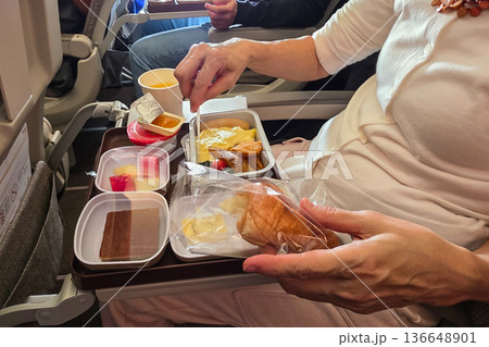 Economy class passenger enjoying meal served in flight in a cramped space Economy class passenger enjoying meal served in flight in a cramped space 136648901