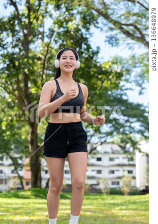 Asian woman in sportswear listening to music in headphones while exercise running or jogging in park Asian woman in sportswear listening to music in headphones while exercise running or jogging in park 136648979