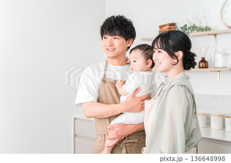 キッチンで赤ちゃんを抱っこするエプロン姿の夫婦,ファミリー 136648998