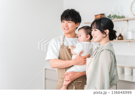 キッチンで赤ちゃんを抱っこするエプロン姿の夫婦,ファミリー キッチンで赤ちゃんを抱っこするエプロン姿の夫婦,ファミリー 136648999