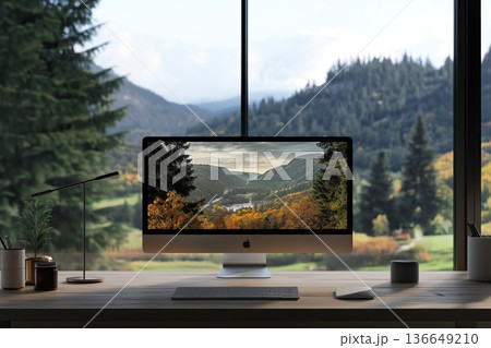 A computer on a desk displays a forest valley scene, framed by a panoramic mountain view through large windows 136649210