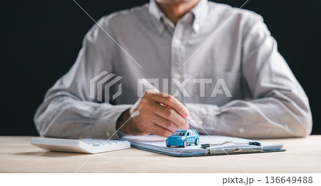 Person prepares to sign auto loan contract, document for car purchase, lease agreement at dealership, finance insurance forms, vehicle sale transaction paperwork, blue car model, calculator on desk 136649488