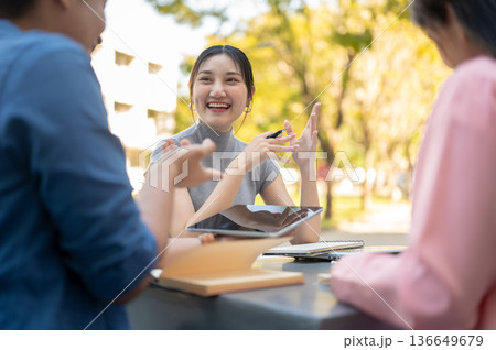Asian woman student hold pen listening to friends talking as working on group project in university. 136649679