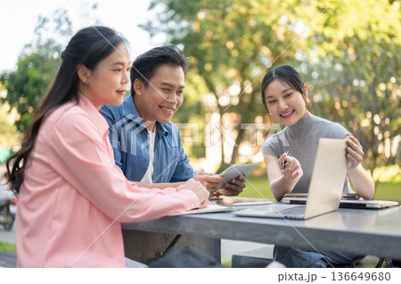 Asian woman student showing laptop to man friend as working on group project at table in university. 136649680