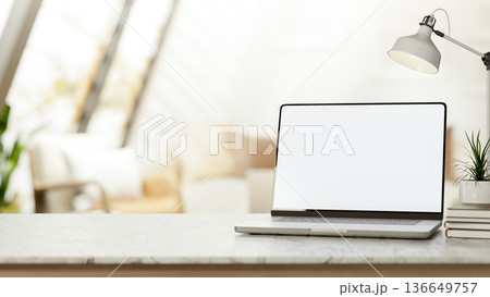 Blank screen laptop with books and plant under lamp on marble counter table in bright living room. Blank screen laptop with books and plant under lamp on marble counter table in bright living room. 136649757