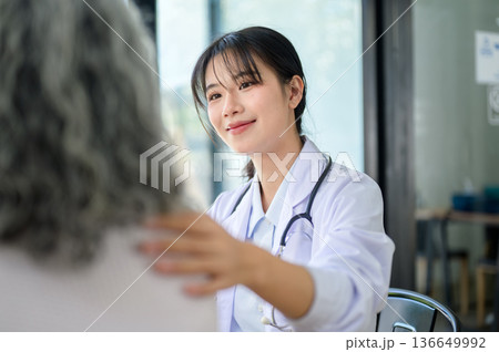 Asian woman doctor touching patting shoulder comforting old patient while sitting in diagnosis room. 136649992