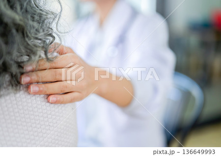 Young woman doctor touching patting shoulder comforting old patient while sitting in diagnosis room. 136649993