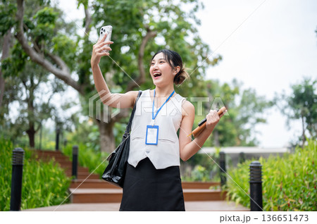 Asian woman office worker holding phone taking picture or video call while walking on stairs in park 136651473