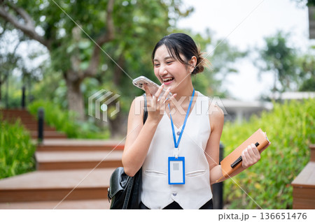 Happy asian woman office worker talking on call closely to phone as walking on wooden stairs in park 136651476