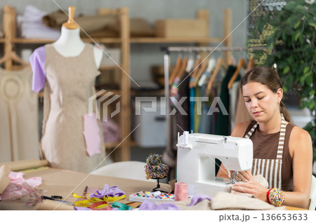 Female seamstress working on a machine against the background of a mannequin 136653633