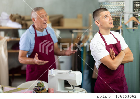 Elderly man scolding young man in sewing workshop Elderly man scolding young man in sewing workshop 136653662