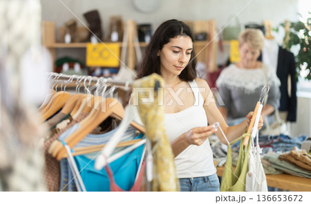 Woman choosing ribbon clothes against the background of a customer in a store 136653672