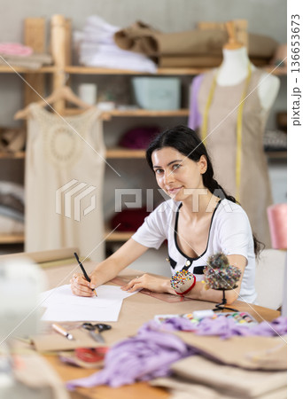 Female tailor drawing sketches of custom garment by hand in studio Female tailor drawing sketches of custom garment by hand in studio 136653673