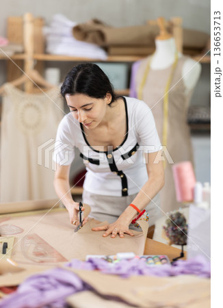 Female fashion maker cutting paper pattern for bespoke garment Female fashion maker cutting paper pattern for bespoke garment 136653713