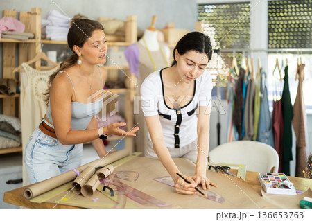 Female seamstresses drafting patterns on paper in sewing workshop Female seamstresses drafting patterns on paper in sewing workshop 136653763