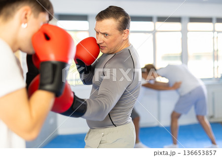 Man and guy at boxing training in gym practice striking techniques. Man put block on blow in his direction 136653857
