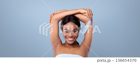 A woman is smiling while holding a feather above her head. She has her arms raised and looks directly at the camera. The background is simple and does not distract from her expression. 136654370