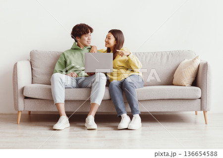 Millennial Asian couple using laptop computer together, sitting on sofa at home, free space. Loving young man and woman having online conference with friends, video chatting with family 136654588