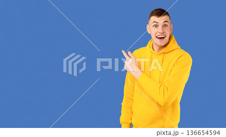 Amazed young caucasian man pointing at copy space for your text or advertisement over blue studio background, showing exciting deal, panorama Amazed young caucasian man pointing at copy space for your text or advertisement over blue studio background, showing exciting deal, panorama 136654594
