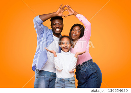 Three people stand together in front of a bright orange background. They share smiles and make gestures with their hands to show love. The atmosphere is joyful and energetic. Three people stand together in front of a bright orange background. They share smiles and make gestures with their hands to show love. The atmosphere is joyful and energetic. 136654620