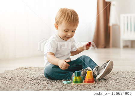 Involved toddler boy with mother playing on floor carpet, using wooden colorful stacking toy, improving fine motor skill of kid. Funny educational games for children concept Involved toddler boy with mother playing on floor carpet, using wooden colorful stacking toy, improving fine motor skill of kid. Funny educational games for children concept 136654909