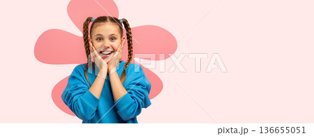 A child smiles broadly while placing her hands on her cheeks. She has two braids and wears a blue top. The background has a simple pink flower design. This moment captures pure delight. A child smiles broadly while placing her hands on her cheeks. She has two braids and wears a blue top. The background has a simple pink flower design. This moment captures pure delight. 136655051