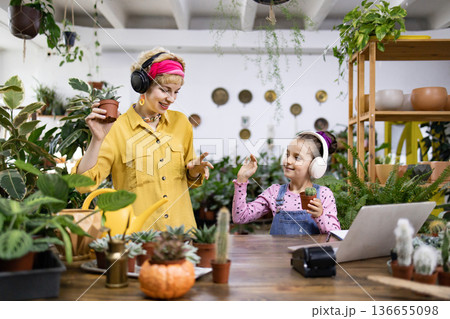A mother and daughter enjoy music while tending to their plants in a bright, inviting space 136655098