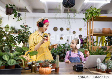 A woman and a girl are in a plant shop, both wearing headphones and looking at plants A woman and a girl are in a plant shop, both wearing headphones and looking at plants 136655109