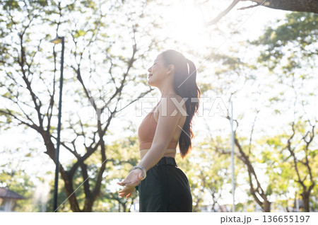 Asian woman in sportswear open arms and standing or resting after exercise in park under sunlight. 136655197