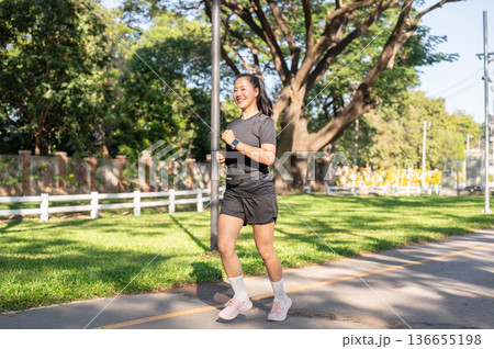 Pretty asian woman in sportswear exercising by running or jogging on the road in park under sunlight Pretty asian woman in sportswear exercising by running or jogging on the road in park under sunlight 136655198
