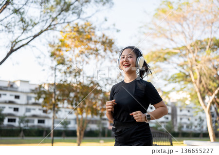 Asian woman in sportswear listening to music in headphone while running jogging exercising in park. Asian woman in sportswear listening to music in headphone while running jogging exercising in park. 136655227