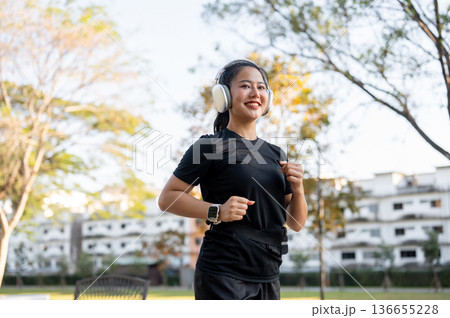 Asian woman in sportswear listening to music with headphone while running jogging exercising in park 136655228