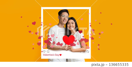 A young couple stands together holding a red heart. They smile at the camera. A background with hearts and a bright color creates a festive mood. The setting shows celebration and joy. 136655335