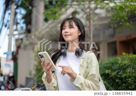 Pretty asian woman tourist looking away from phone while standing or walking traveling by local road Pretty asian woman tourist looking away from phone while standing or walking traveling by local road 136655441