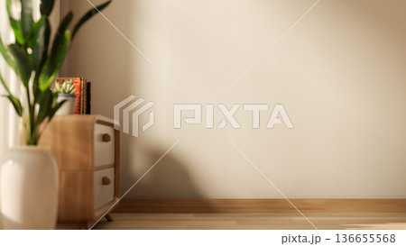 Books and potted plant on wooden drawer table and vase on parquet floor with sunlight through window 136655568