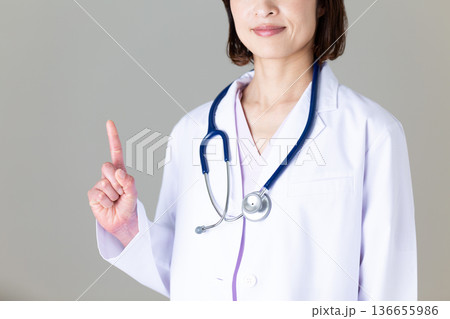 人差し指を立てる白衣姿のミドル女性医師 136655986