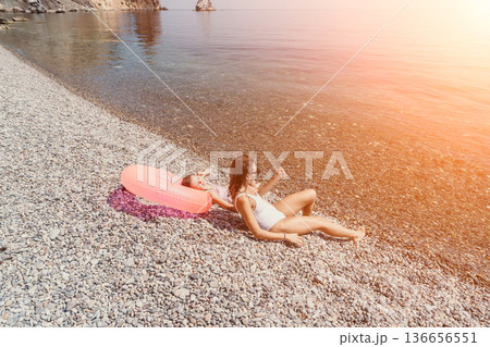 Mother child beach relaxing on a pebble shore with a pink inflatable ring during a sunny summer vacation 136656551