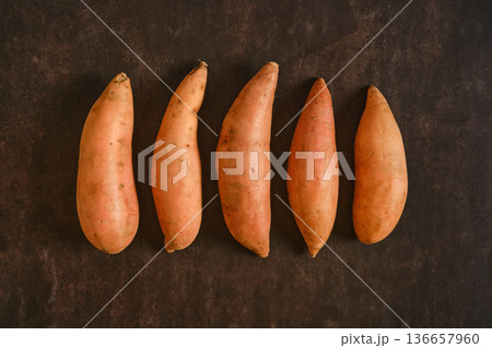 Sweet potatoes lined up on a dark surface ready for cooking or baking 136657960