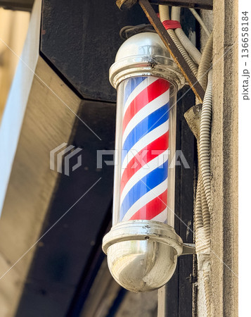 Close-up traditional barber pole with red, blue and white stripes mounted on a wall. Urban tradition, retro style and classic grooming culture. Close-up traditional barber pole with red, blue and white stripes mounted on a wall. Urban tradition, retro style and classic grooming culture. 136658184